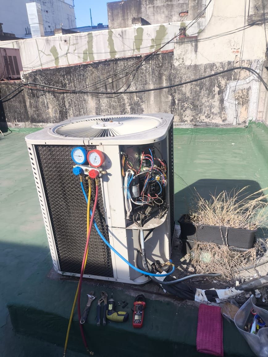 Unidad exterior con la tapa del tablero abierta, mostrando el cableado y el capacitor, con manómetros y pinza amperométrica