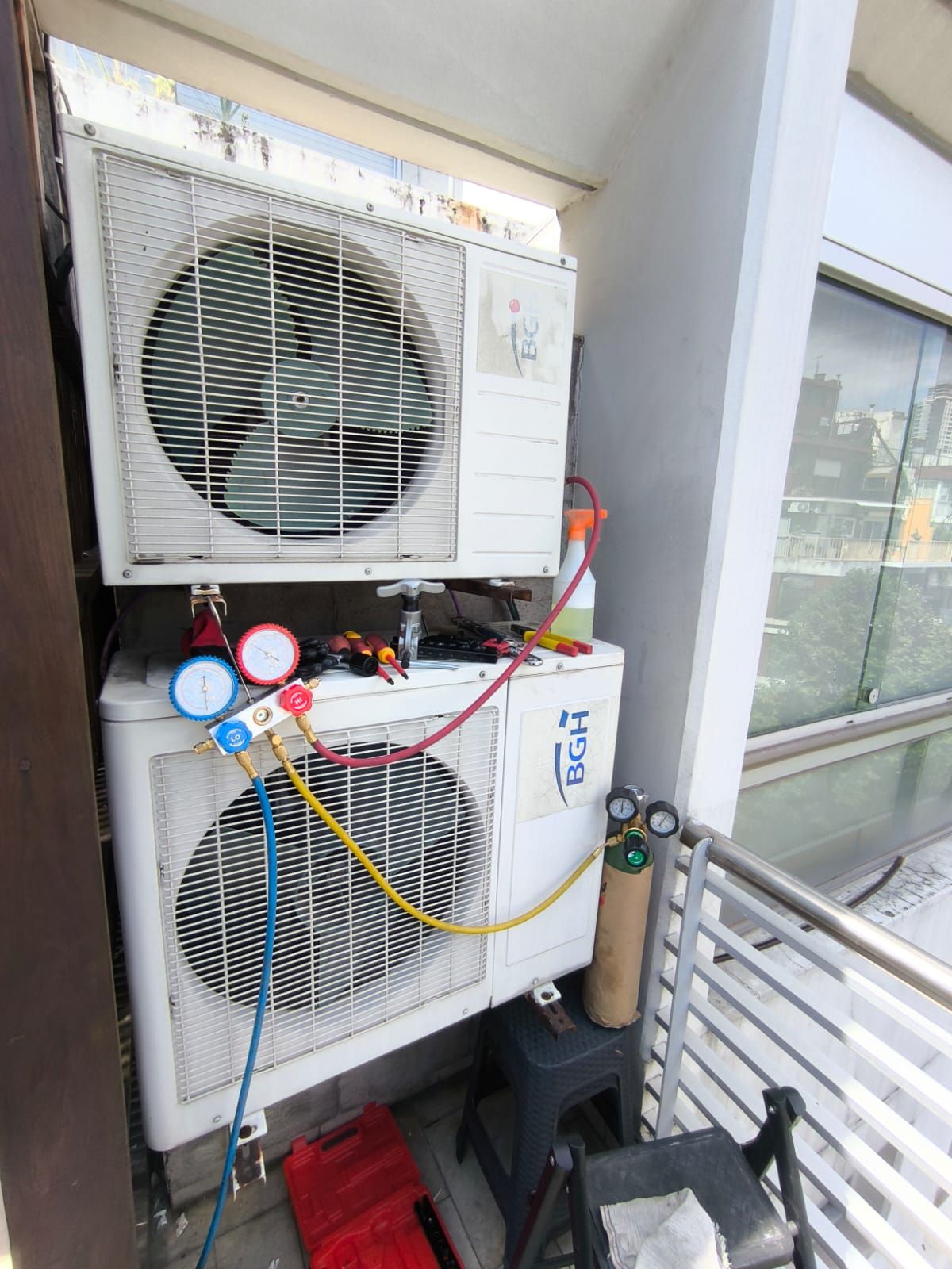 Dos unidades exteriores montadas una sobre otra en un balcón, con los manómetros conectados y la garrafa de gas al costado