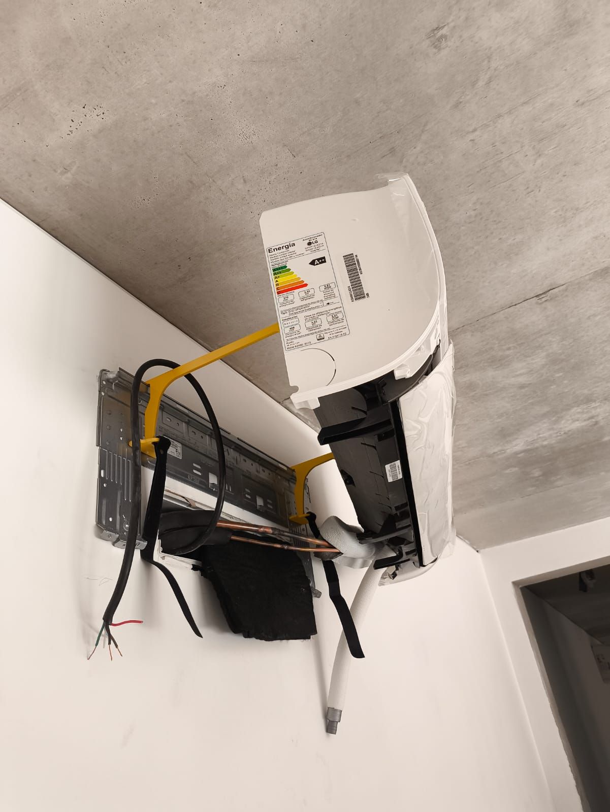 Unidad interior nueva colocada sobre su soporte de pared, con la cañería, el desagote y el cable todavía a la vista